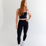 Alt text: "A woman is modeling Rae Butter Collection black leggings from Raeya Fit. These high-waisted leggings are crafted from a soft and comfortable fabric, providing a sleek and form-fitting look. Perfect for both workouts and casual wear, the leggings are showcased against a minimalist white background."