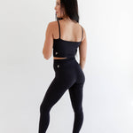Alt text: "A woman is showcasing the best-selling Rae Butter Collection black leggings from Raeya Fit. These 5-star reviewed leggings feature a 28" inseam suitable for all heights, a Glute-Curve back seam to accentuate the booty, no front or side seams, and a high-waisted design with a double-lined hip band to ensure they stay in place. Made from soft and comfortable fabric, they offer a sleek, form-fitting look perfect for any activity."