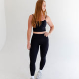 Alt text: "A woman is modeling Rae Butter Collection black leggings from Raeya Fit. These high-waisted leggings are crafted from a soft and comfortable fabric, providing a sleek and form-fitting look. Perfect for both workouts and casual wear, the leggings are showcased against a minimalist white background."