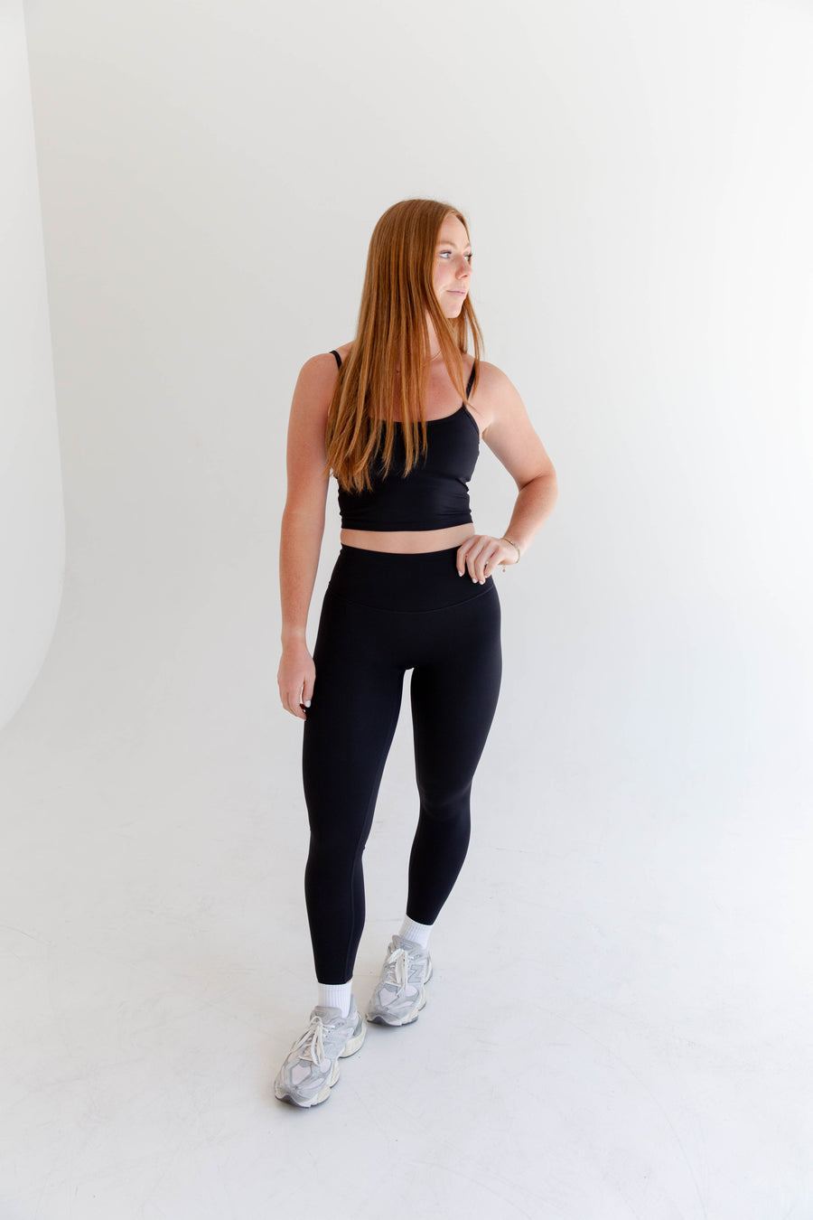 Alt text: "A woman is modeling Rae Butter Collection black leggings from Raeya Fit. These high-waisted leggings are crafted from a soft and comfortable fabric, providing a sleek and form-fitting look. Perfect for both workouts and casual wear, the leggings are showcased against a minimalist white background."