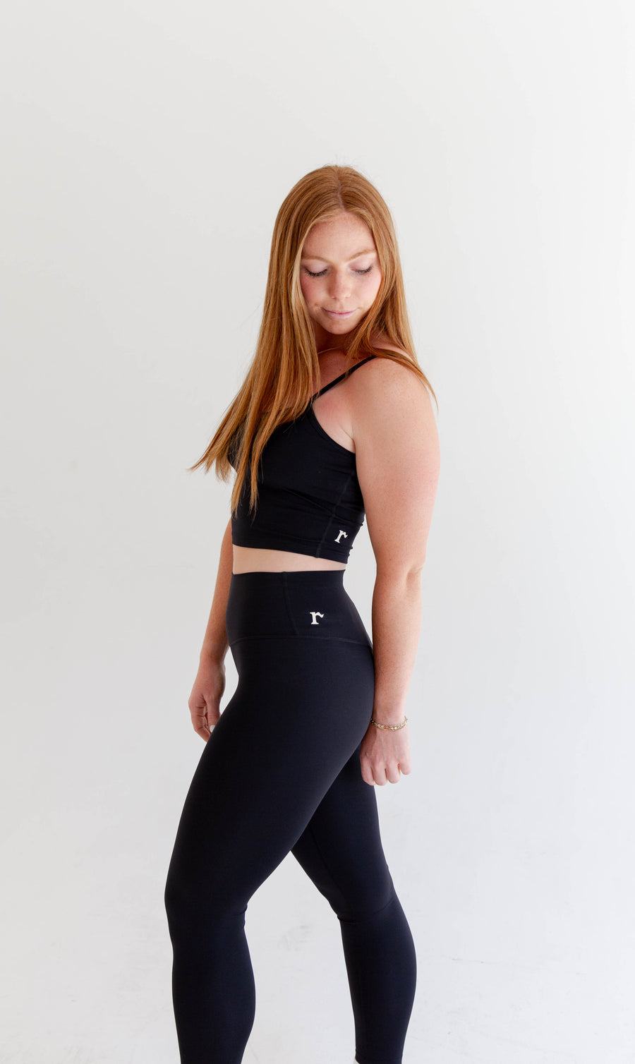 Alt text: "A woman is modeling Raeya Fit's best-selling Rae Butter Collection black leggings, renowned for their 5-star reviews. These high-waisted leggings feature a 28" inseam to fit all heights, a Glute-Curve back seam to enhance the booty, and no front or side seams for a sleek silhouette. The double-lined hip band ensures they stay in place during workouts. Made from ultra-soft, comfortable fabric, these leggings are perfect for both exercise and everyday wear."